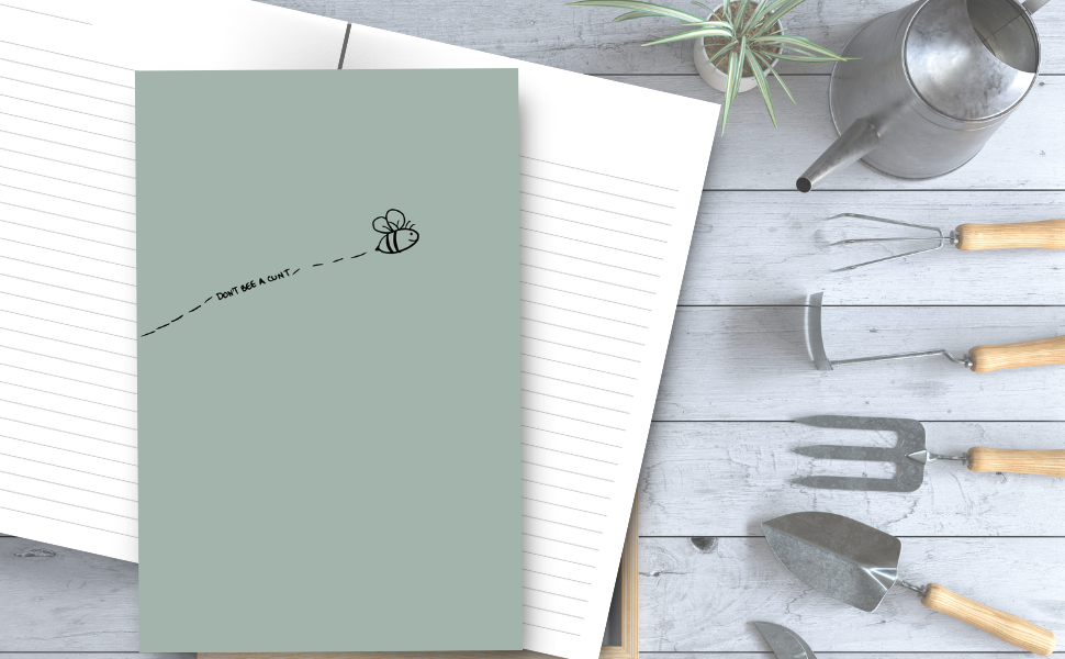 Don't bee a cunt notebook with an adorable bumble bee, inside pages, on a table with a plant and gardening tools.