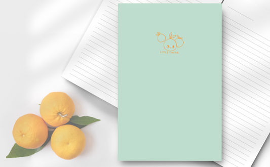 soft green cover of notebook, with 3 little oranges, one with a cute smiling face with the words below 'little cuntie'.