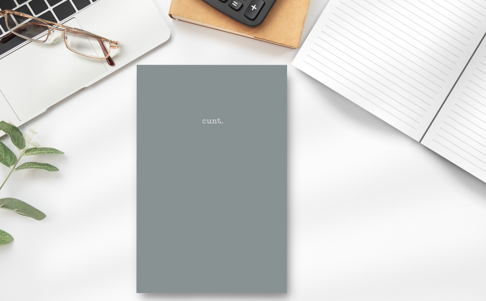 This image features a sleek, granite-grey notebook with the word "cunt." subtly printed at the top. On a desk showing the inside lined pages, laptop, calculator and plant.