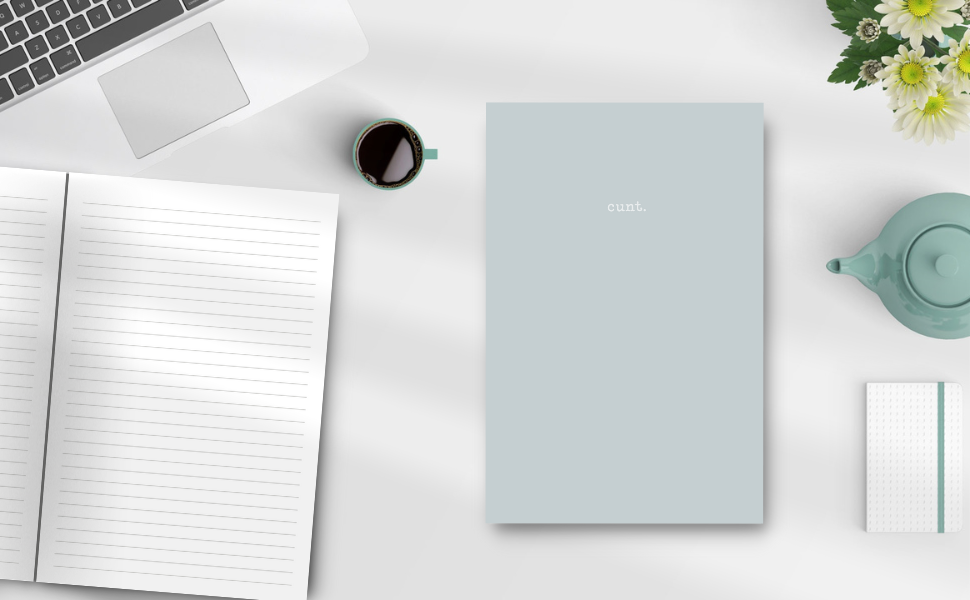 Sage grey colour notebook with the word cunt. on a desk showing the inside pages, keyboard, tea pot, flowers