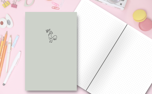 Notebook cover with a hand-drawn illustration of a rooster in a minimalist style saying 'cunt-a-doodle-doo'. Inside dot grid pages on a fun pink background, pencils, pens, erasers, paper clips.