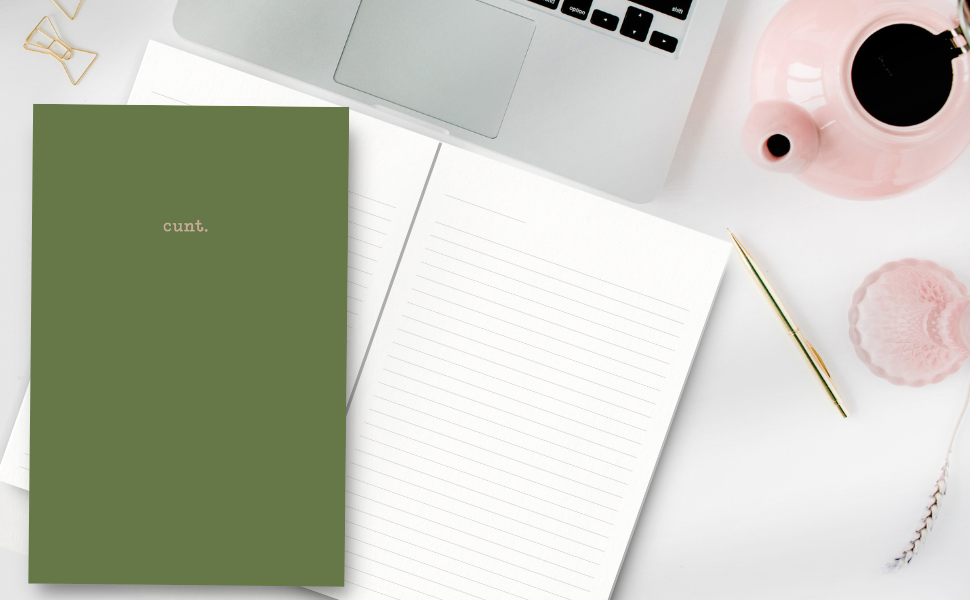Green notebook with 'cunt' on a desk with a laptop and a tea pot.